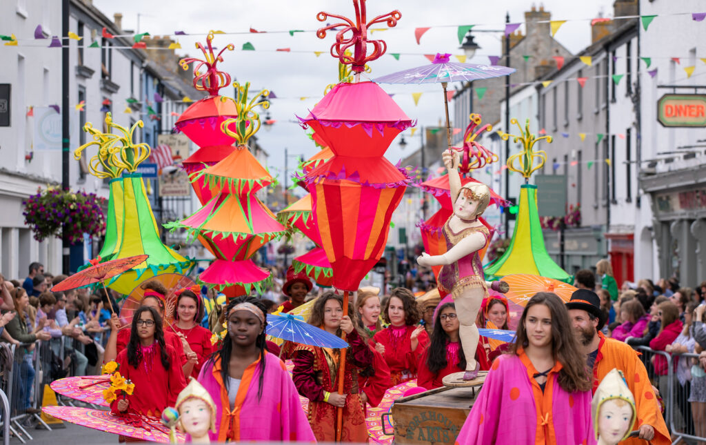 Birr Vintage Week Parade. Young people dressed in colourful costumes holding props such as colourful parasols walking along main street Birr.  Crowds of people looking on from each side of the street.