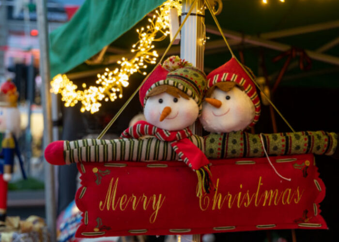 Two Plush Snowmen On A Merry Christmas Sign