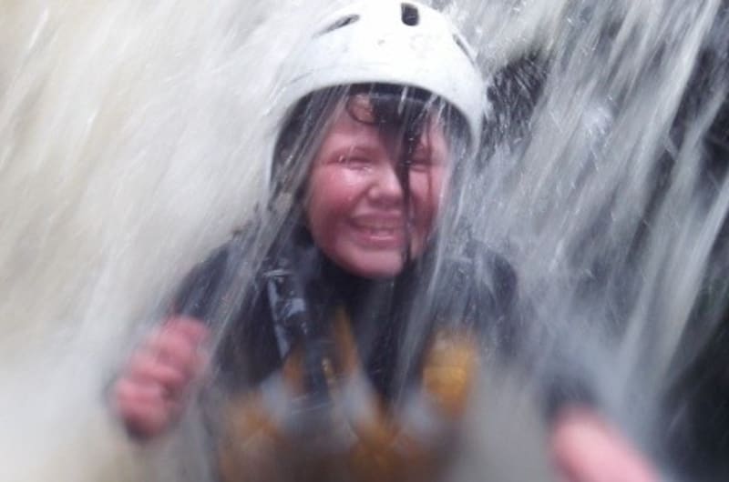 Child Smiling Under Waterfall Wearing White Helmet