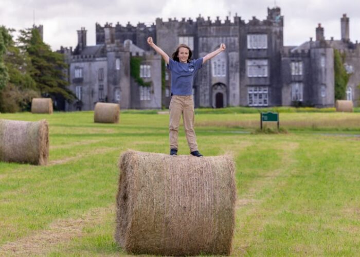 Child standing on hay bale before a castle