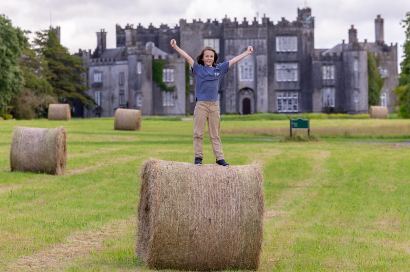 Child standing on hay bale before a castle