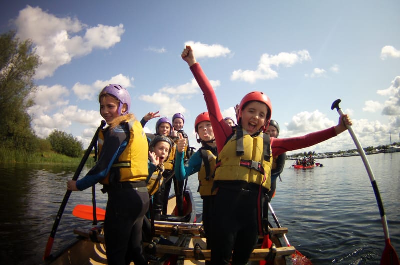 Children wearing life jackets cheering in a canoe
