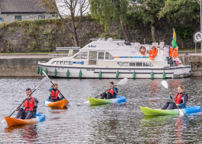 Four Kayakers Paddling In River Near Boat