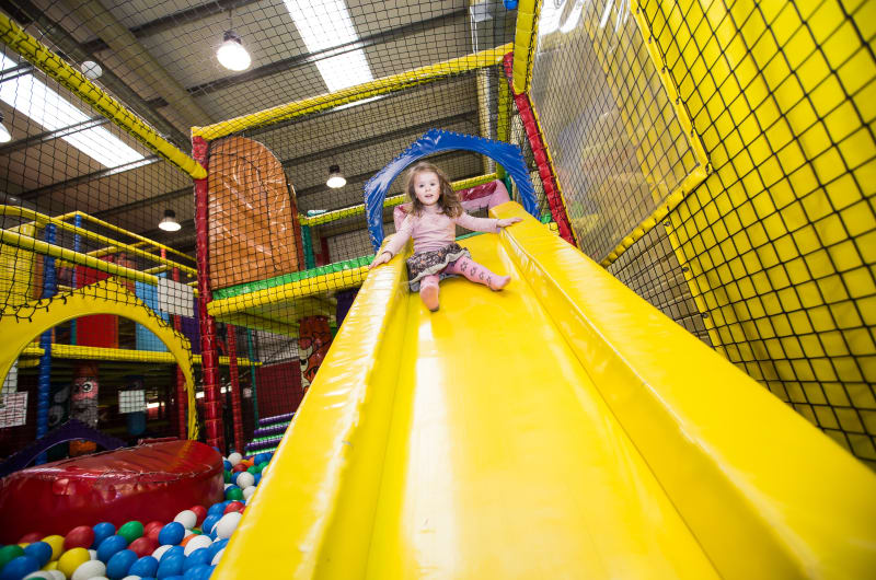 Girl Sliding Down Yellow Slide In Indoor Playground