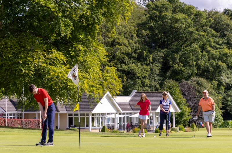 Golfer putting on green with spectators and clubhouse
