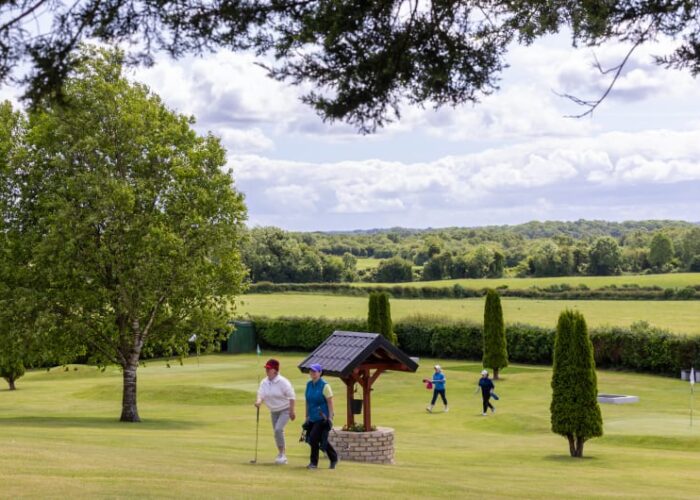 Golfers Walking On Green Course Near Ornamental Well
