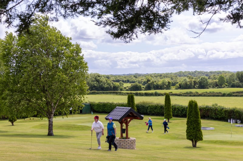 Golfers Walking On Green Course Near Ornamental Well