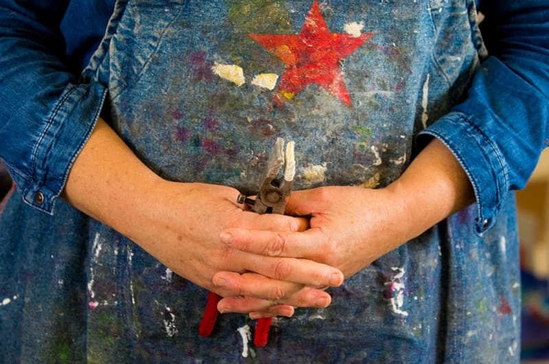 Hands Holding Pliers Over Paint Splattered Star Apron
