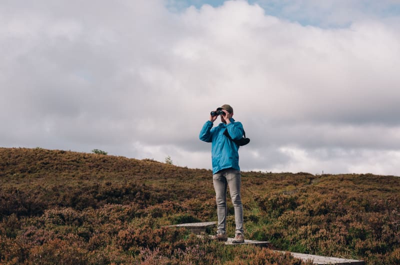 Man Looking Through Binoculars On Hilly Path