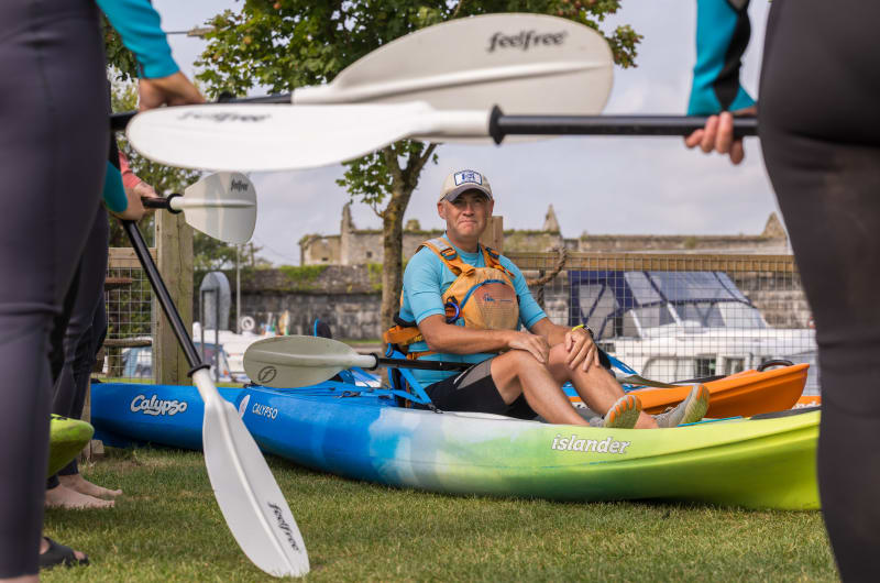 Man Sitting In Kayak Surrounded By Held Paddles