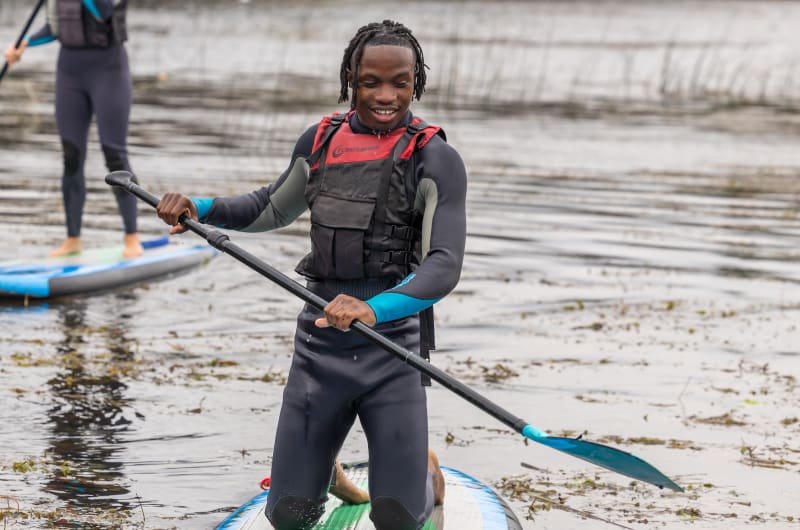 Man Wearing Wetsuit Kneeling On Paddleboard