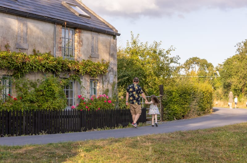 Man and girl walking past stone house
