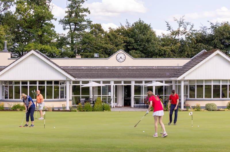 People Putting On A Golf Green Near Clubhouse