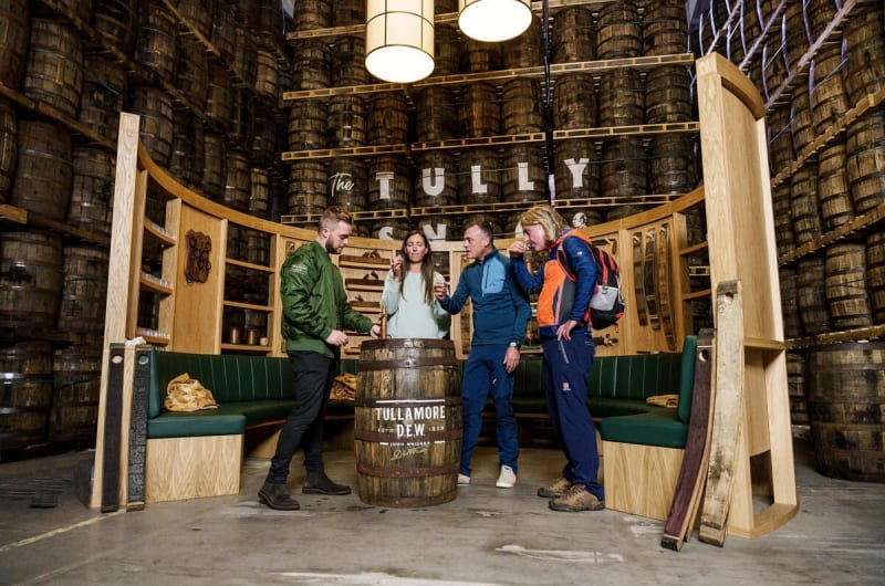 People Tasting Whiskey Around Barrel In Distillery Warehouse