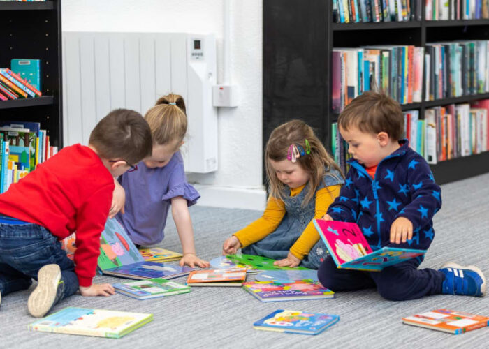 Preschool Children Sitting On Library Floor Reading Books vtiqf1