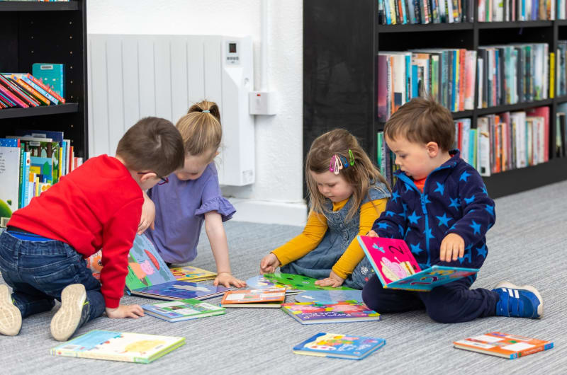Preschool Children Sitting On Library Floor Reading Books vtiqf1