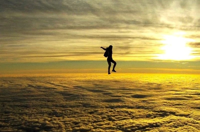 Silhouette Of Skydiver Jumping Over Clouds At Sunset