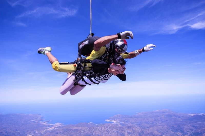 Tandem Skydivers Freefalling Over Coastal Landscape