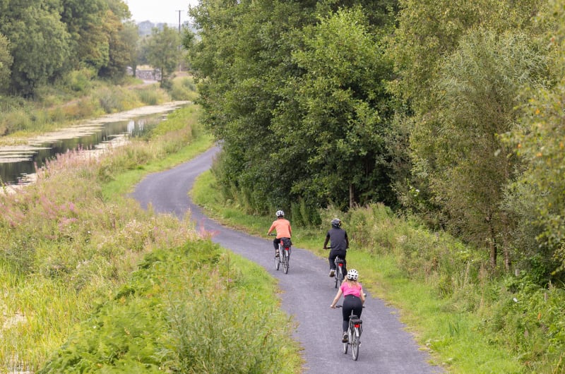Three people cycling on scenic canal path