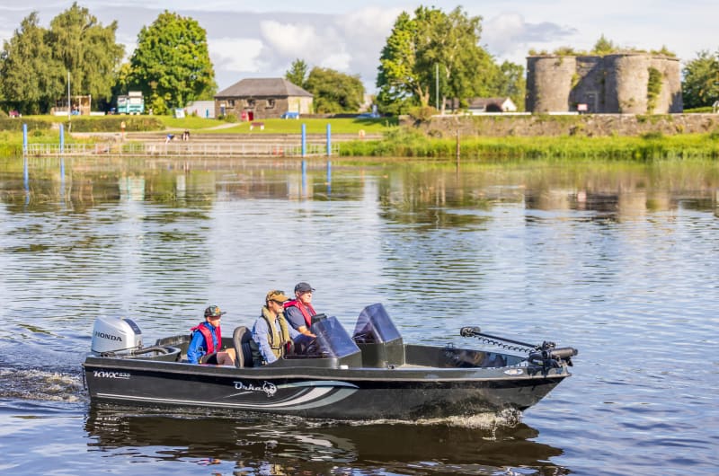 Three people in motorboat on river near ruins