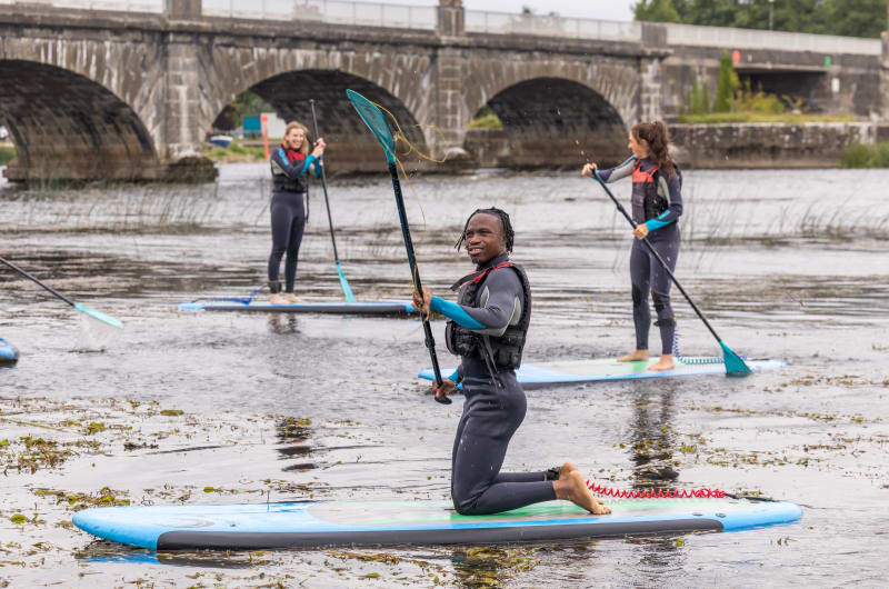 Three people paddleboarding on river near bridge