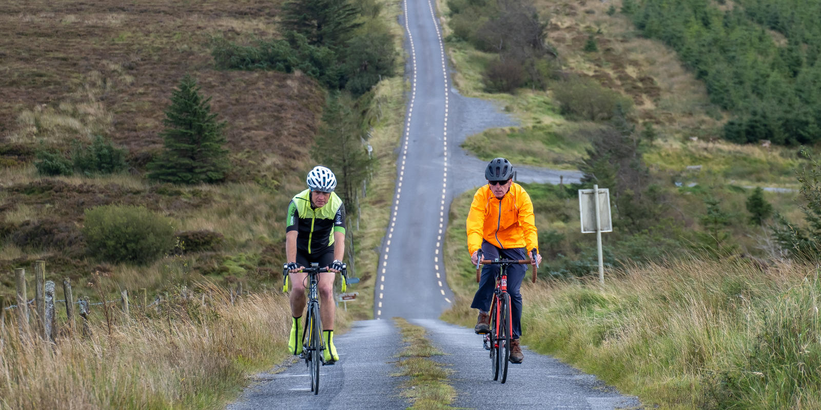 Two Cyclists Riding On A Long Hilly Road hd6j0j
