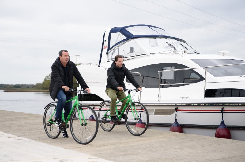 Two Men Riding Green Bicycles Beside Luxury Yacht