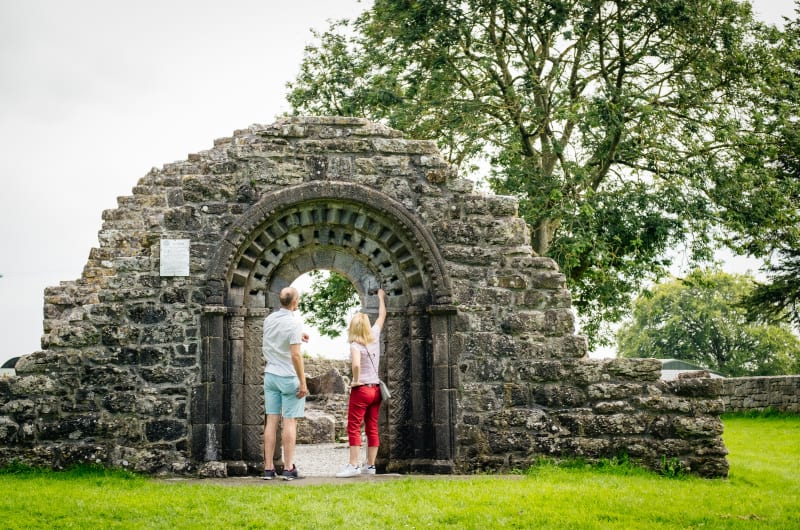 Two People Looking At Carved Stone Ruin Archway