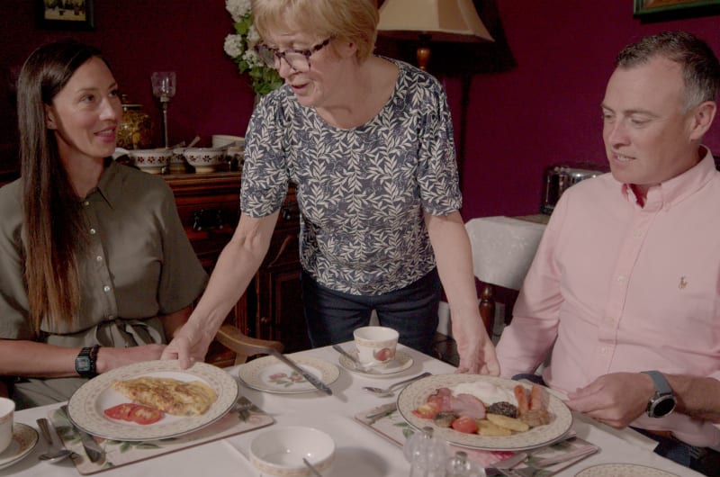 Woman Serving Breakfast To Two People At Table