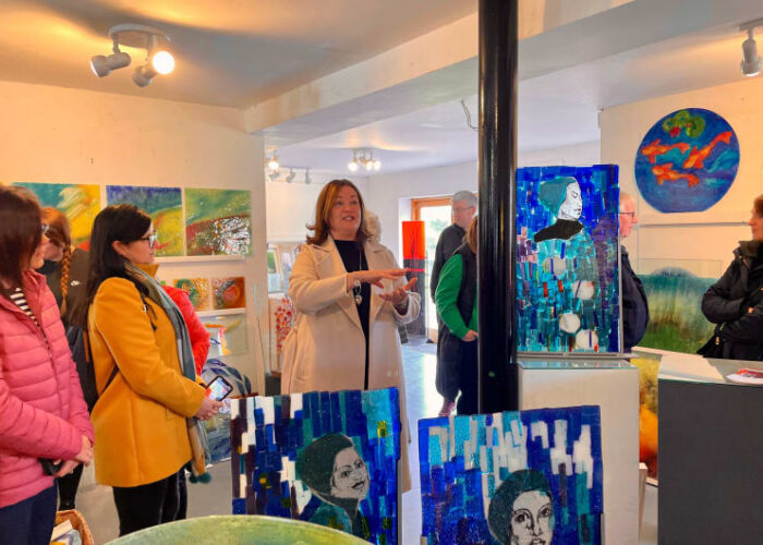Woman Speaking To Group In Glass Art Gallery