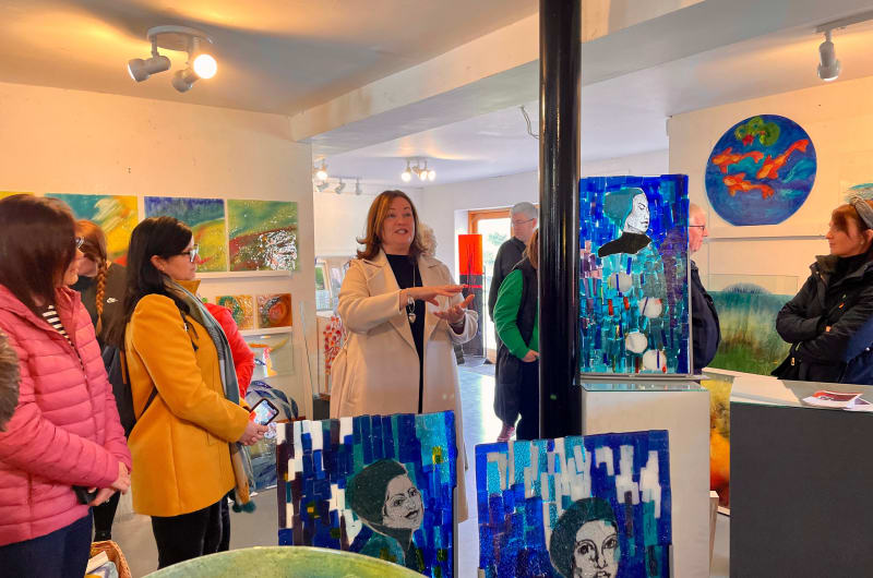 Woman Speaking To Group In Glass Art Gallery