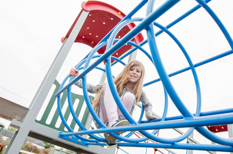 Young Girl Playing On Blue Playground Climbing Structure