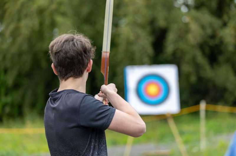 Young Man Aiming Bow At Archery Target Outdoors