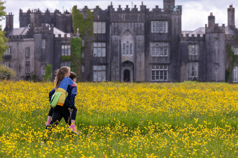 girl and boy horsey back across flowery field by castle