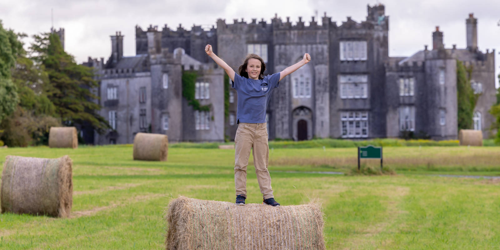 header child standing on haybail in front of castle
