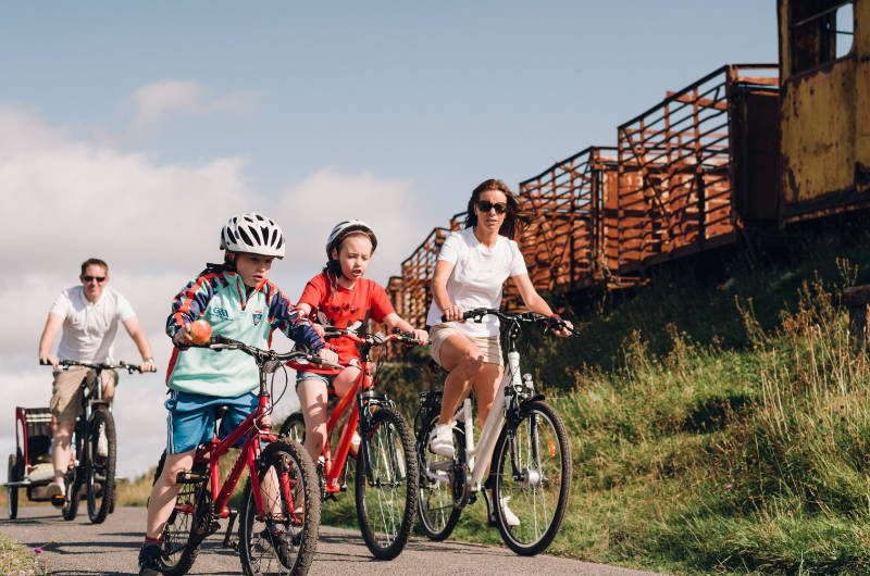 park family cycling past rusty train