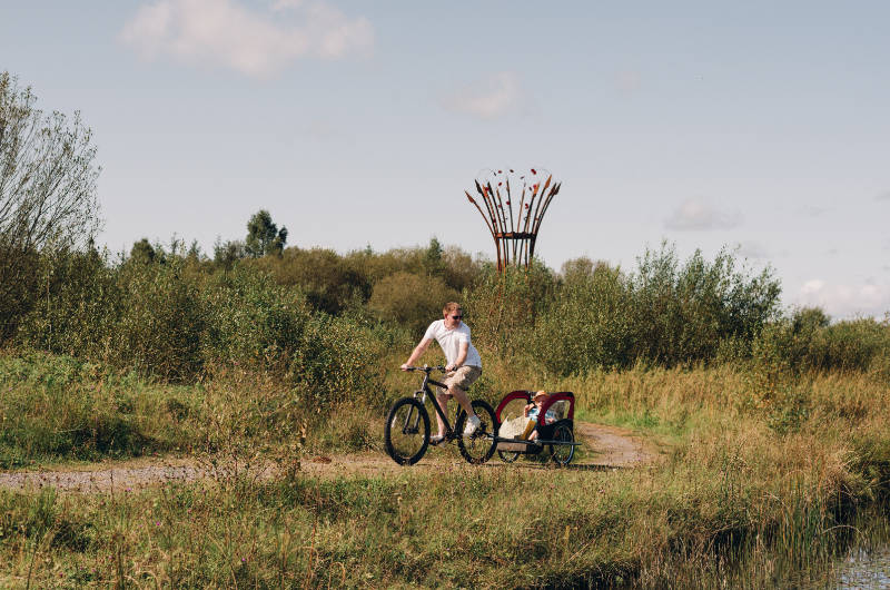 park father and family on bike passing sculpture