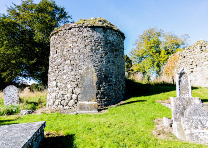 Ancient stone round tower in cemetery with tombstones
