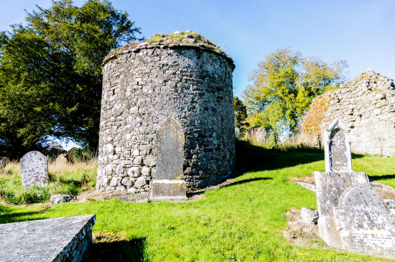 Ancient stone round tower in cemetery with tombstones
