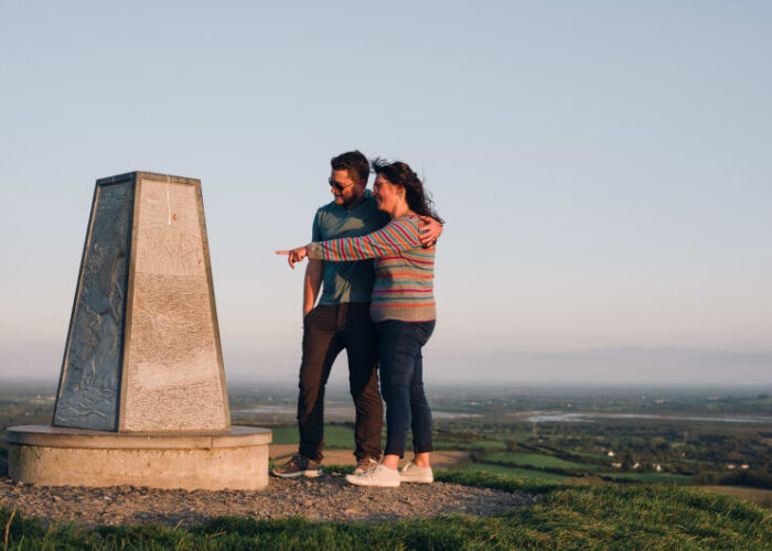 Couple Standing By Stone Monument Overlooking Scenic Valley uiurpp