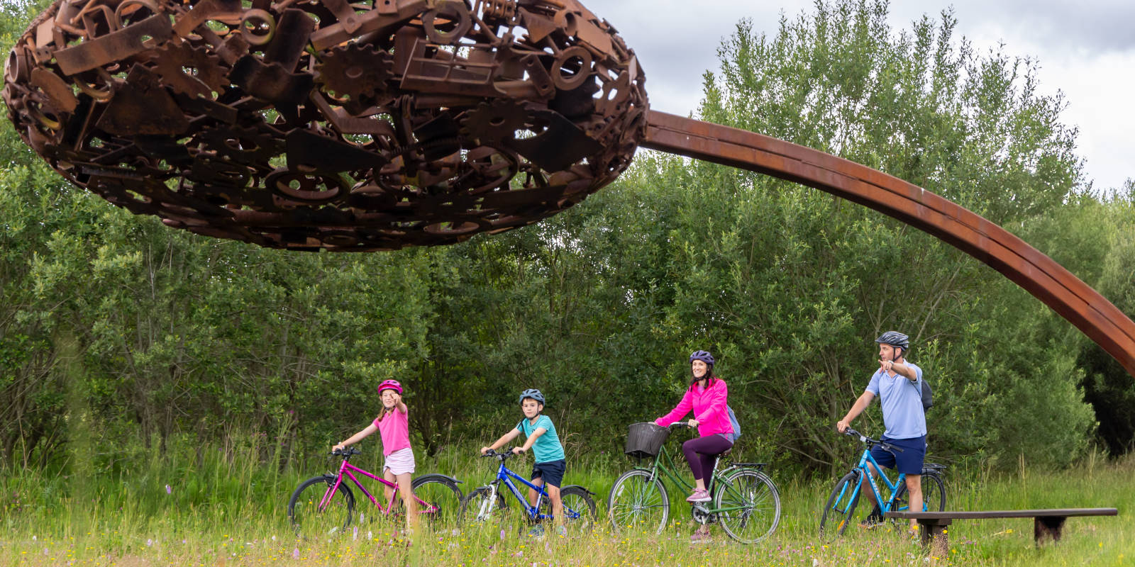 Family Cycling Under Large Scrap Metal Sculpture