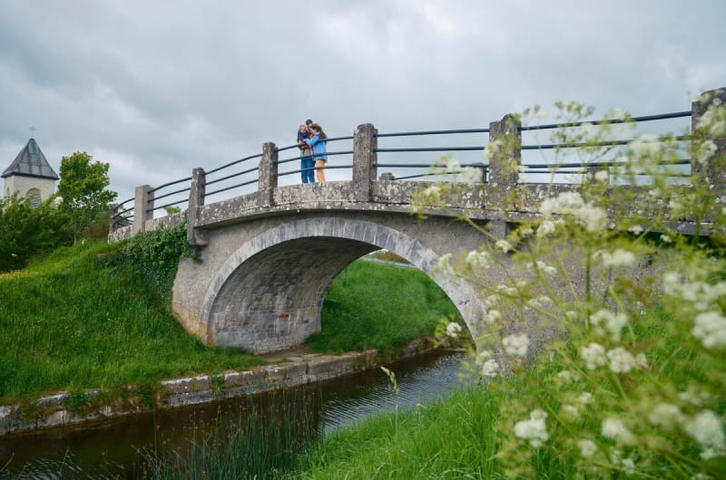Family standing on arched stone bridge over canal vfbcqm