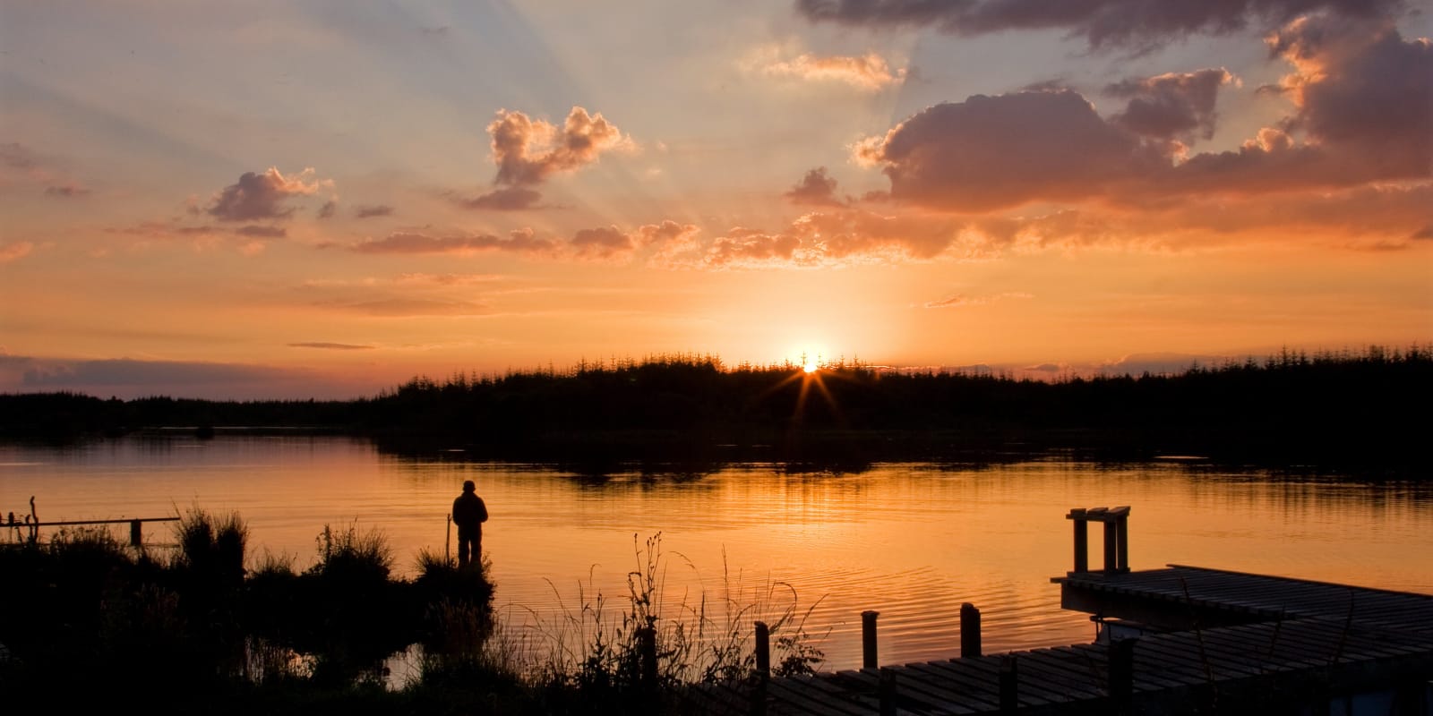 Fishing Header Image Sunset over lake with silhouetted person and dock