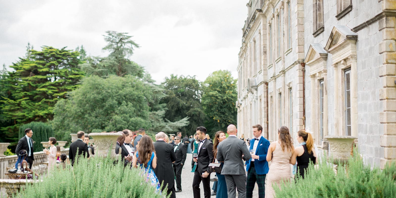 Formal event guests socializing outside a historic manor