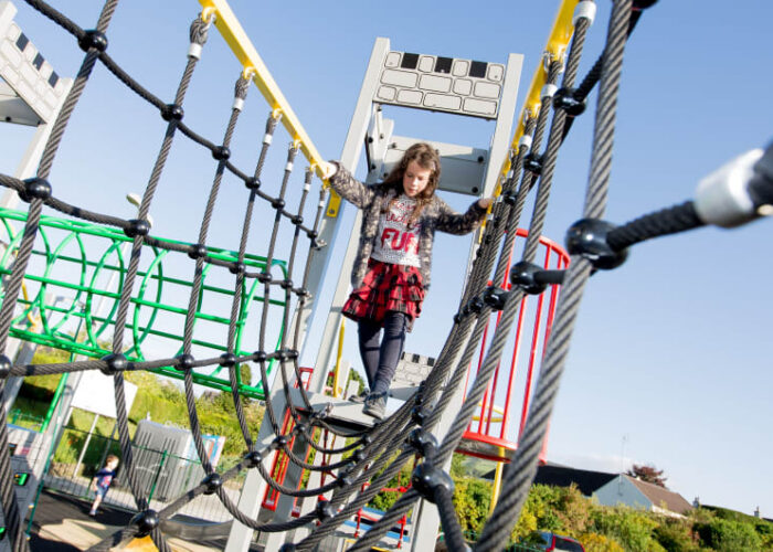 Girl climbing rope bridge on playground structure mz7byx