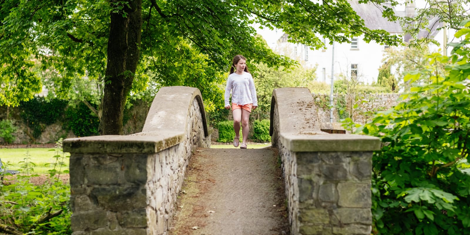 Kilcormac Header Image Young Girl Walking Across A Stone Park Bridge