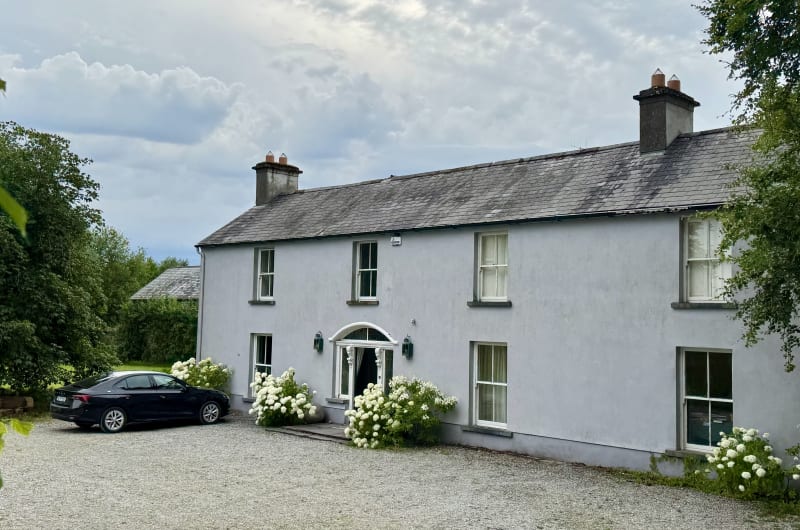 Large grey house with gravel driveway and car