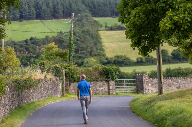 Man Walking Away On Countryside Road With Hills vpnoik