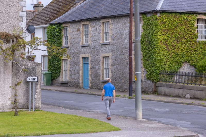 Man Walking Past Ivy Covered Stone Buildings opgx4h