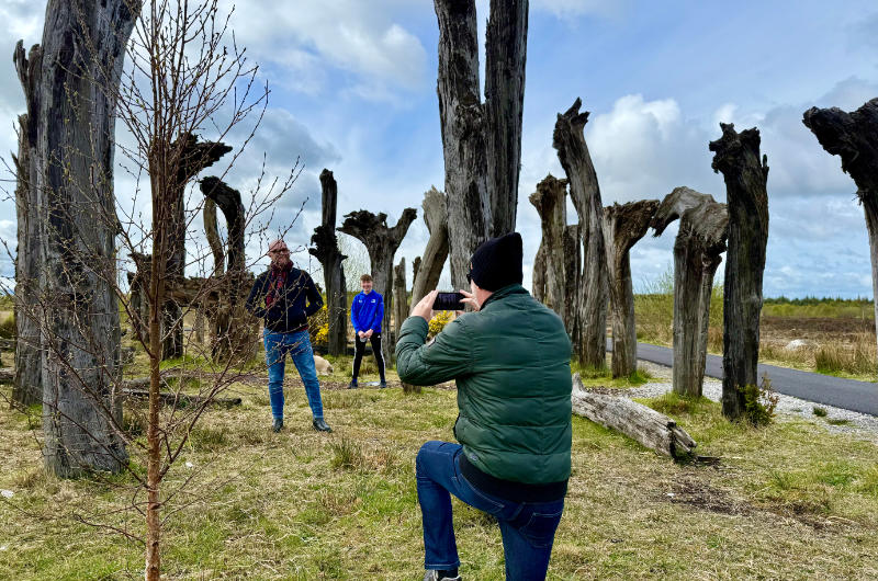 Man taking photo of people among wooden sculptures